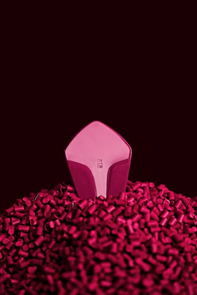 Close-up vertical shot of a pink 3D printed object on magenta plastic pellets, against a black background.